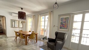 Un amplio salón con una mesa de comedor de madera y sillas amarillas, un sillón de cuero negro y un ventanal con cortinas.