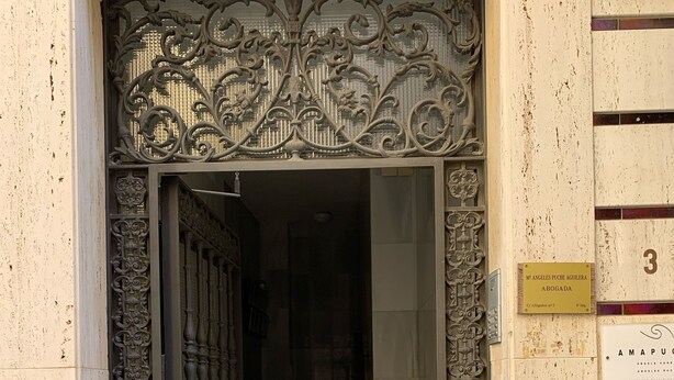 Una entrada de edificio con puertas de metal ornamentadas, una escalera que lleva al interior y un letrero que indica el nombre del edificio.