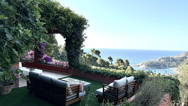 A patio with a wooden bench and a cushioned seating area, overlooking a coastal landscape with a clear view of the sea and distant hills. - Holiday rental villa with swimming pool in Begur, Aiguablava (Begur)