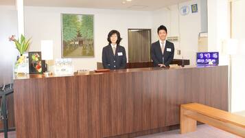 A reception desk with a wooden finish, a digital clock displaying the time, and a framed painting on the wall.