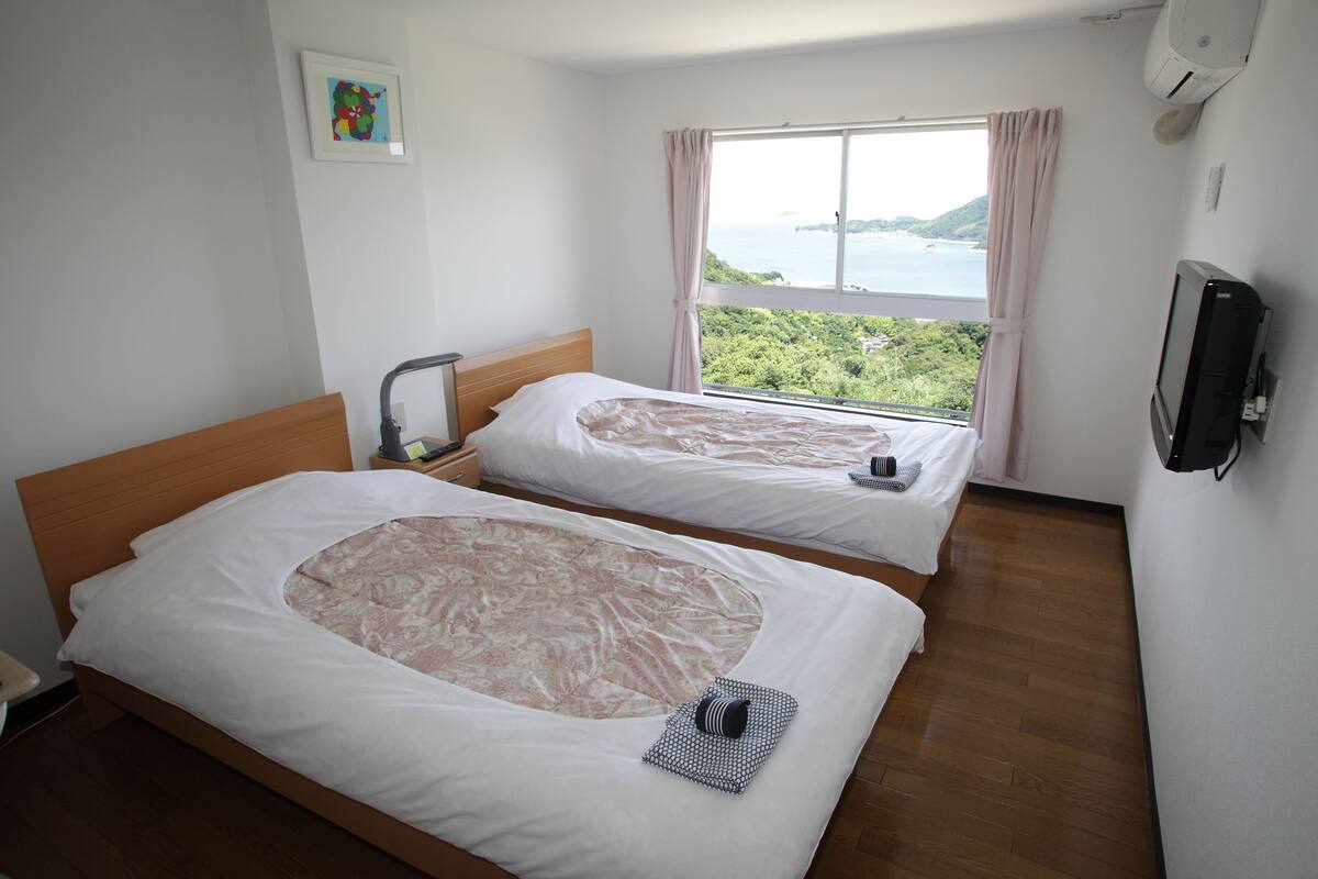 Camera d'albergo con due letti, vista mare e televisore a parete.