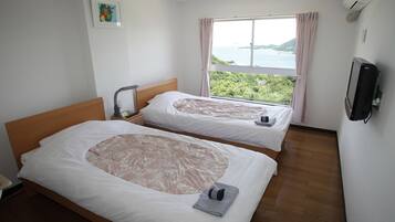 Habitación de hotel con dos camas, vista al mar y un televisor en la pared.