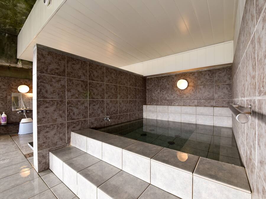 A modern bathroom with a large bathtub, tiled walls, and a step leading into the tub.