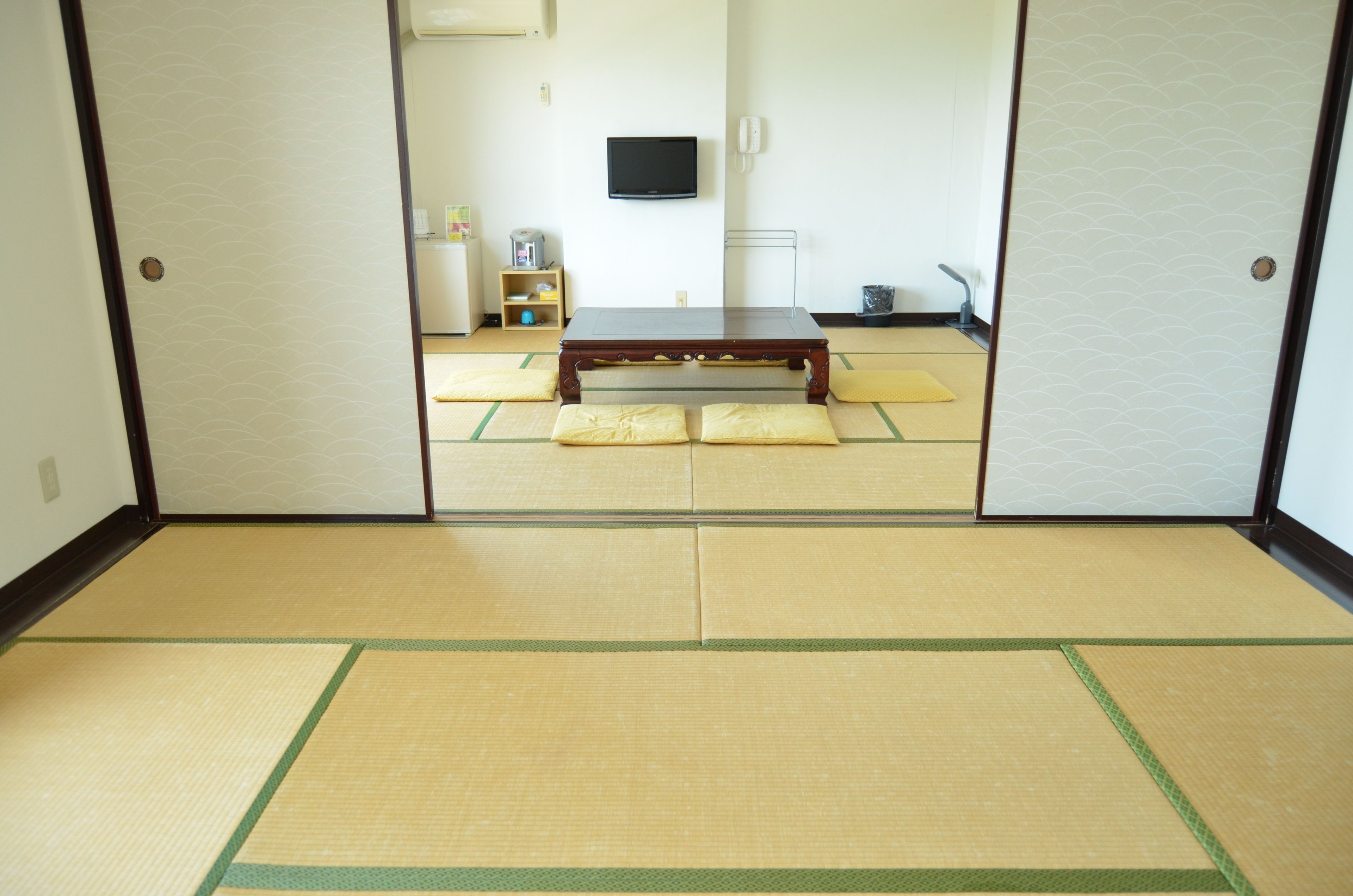 Una habitación japonesa tradicional con suelo de tatami, una mesa de madera baja y un televisor en la pared.