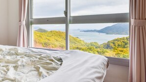 Un dormitorio con un amplio ventanal que ofrece vistas a un paisaje montañoso y una masa de agua.