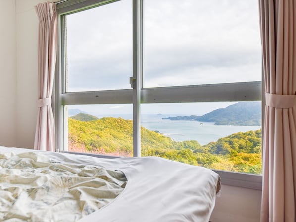 Un dormitorio con un amplio ventanal que ofrece vistas a un paisaje montañoso y una masa de agua.