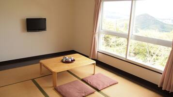 Una habitación con suelo de tatami, una mesa de madera baja y un televisor en la pared.
