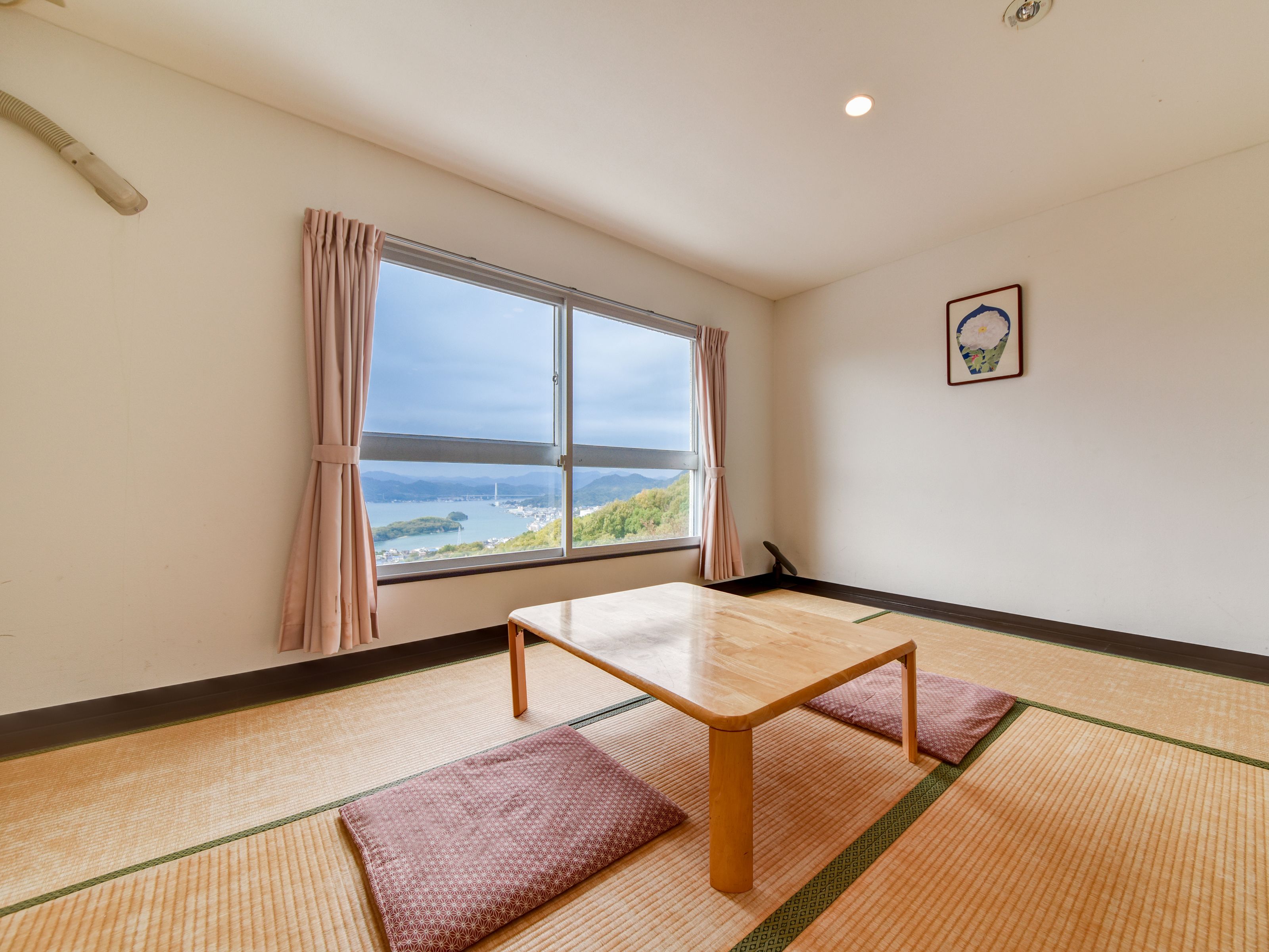 A room with tatami mats, a wooden table, and a view of a body of water and mountains.