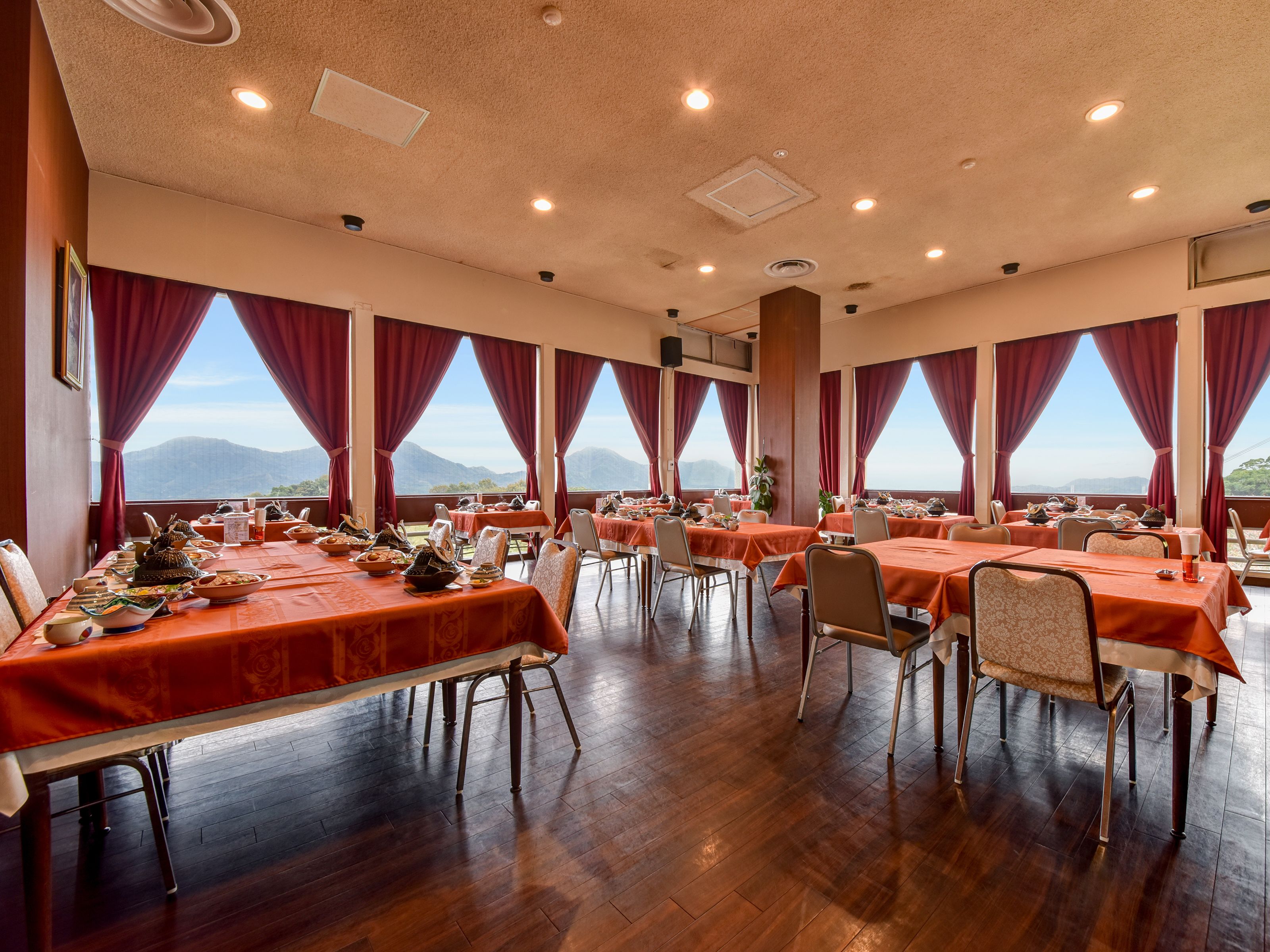A large dining hall with multiple tables, red curtains, and a view of mountains.