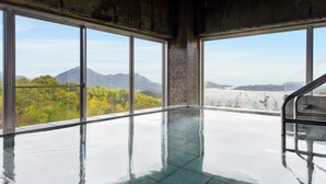 Una amplia piscina interior con grandes ventanales que ofrecen vistas a montañas y vegetación.