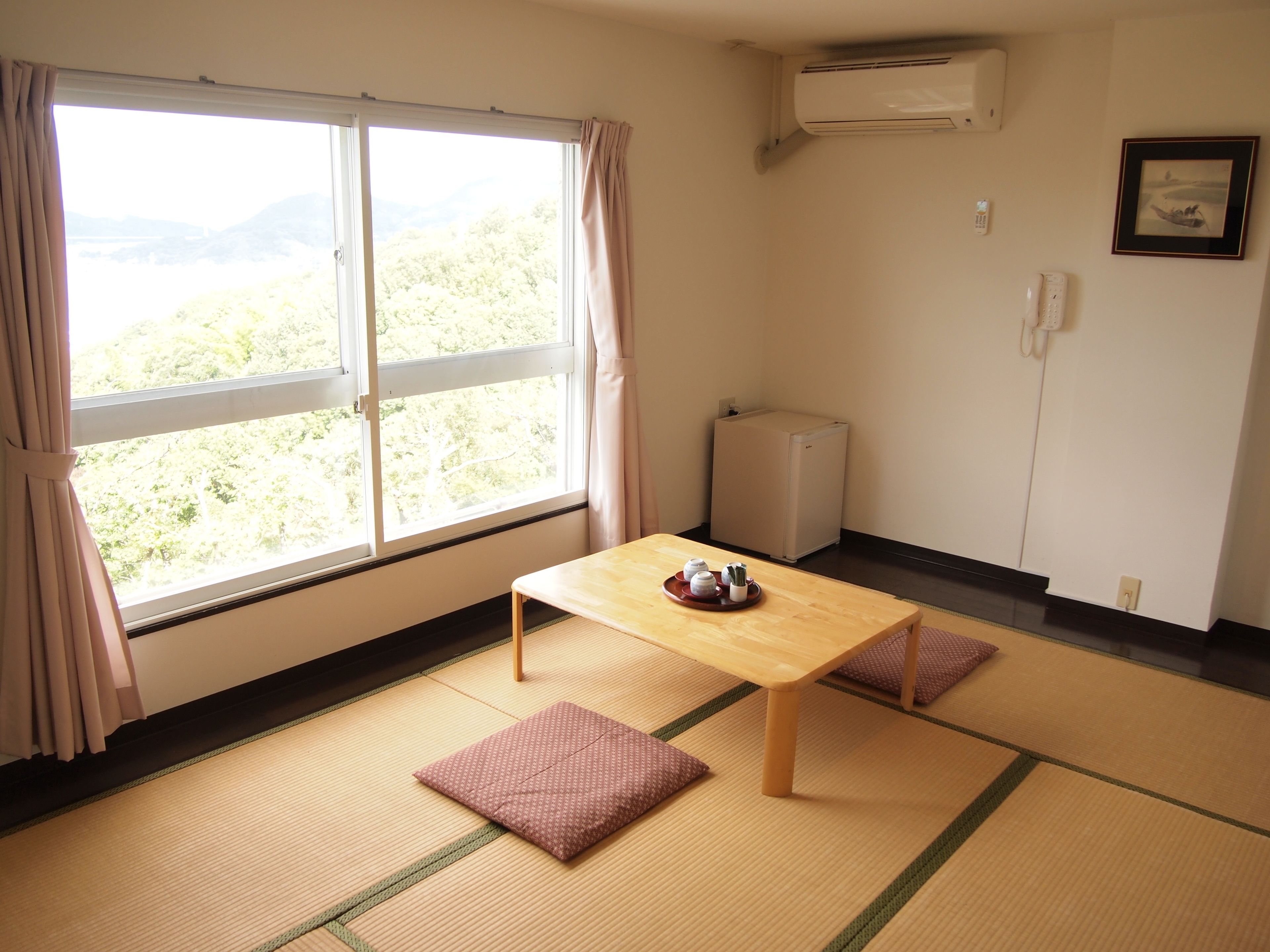 A room with tatami flooring, a low table with a tray of items, a radiator, and a window with curtains.