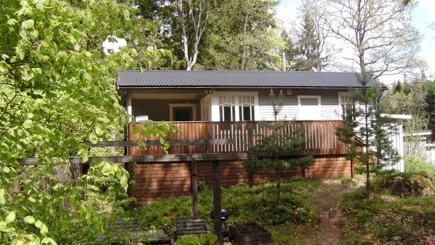 Una casa con terraza de madera, porche cubierto y patio cercado.
