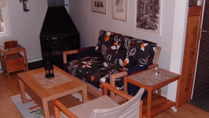 Una sala de estar acogedora con un sofá, dos mesas de madera, una silla y una chimenea.