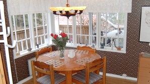 Un comedor con una mesa redonda de madera, cuatro sillas, un florero con flores y una araña.