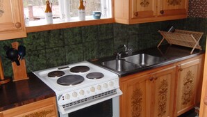 Una cocina con estufa blanca, gabinetes de madera, un lavamanos y una ventana decorada.