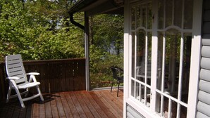 Terraza de madera con una silla blanca y una mesa, con vistas a un paisaje verde y exuberante.
