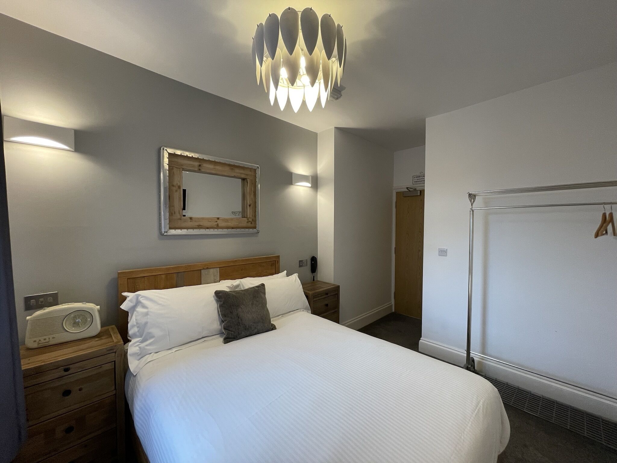 A neatly arranged bedroom with a bed, bedside tables, a radio, a mirror, and a wardrobe.