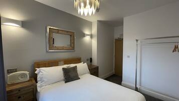 A neatly arranged bedroom with a bed, bedside tables, a radio, a mirror, and a wardrobe.