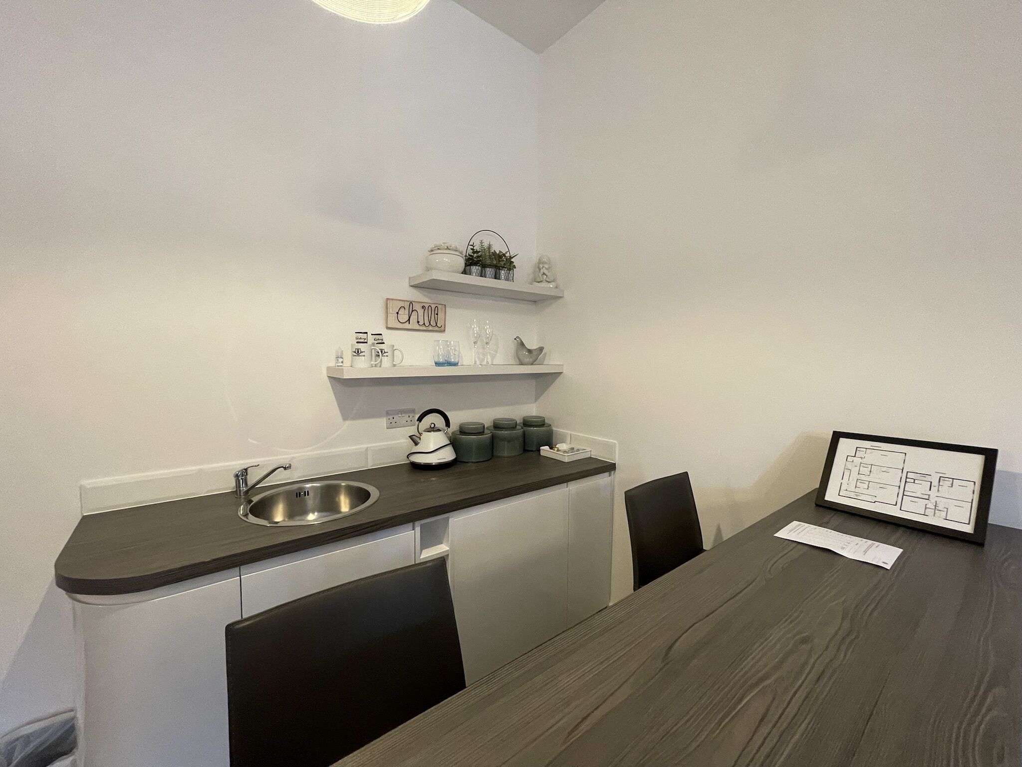 A compact kitchen with a sink, kettle, and shelves with decorative items.