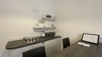 A compact kitchen with a sink, kettle, and shelves with decorative items.