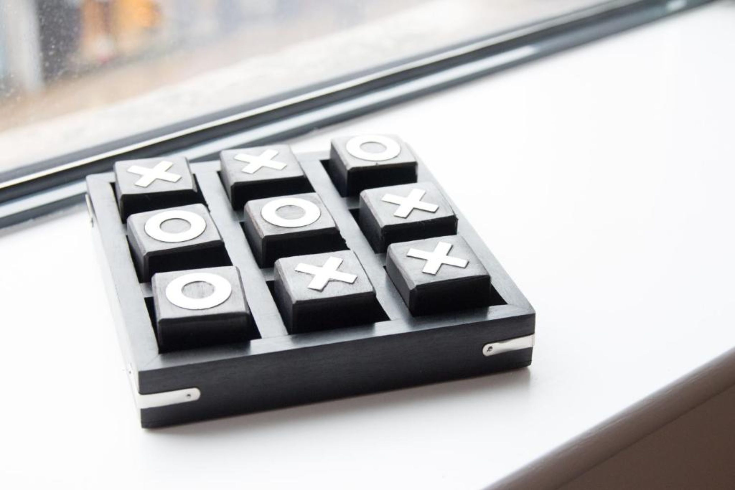 Un jeu de plateau noir et blanc avec les symboles « X » et « O », posé sur un rebord de fenêtre.