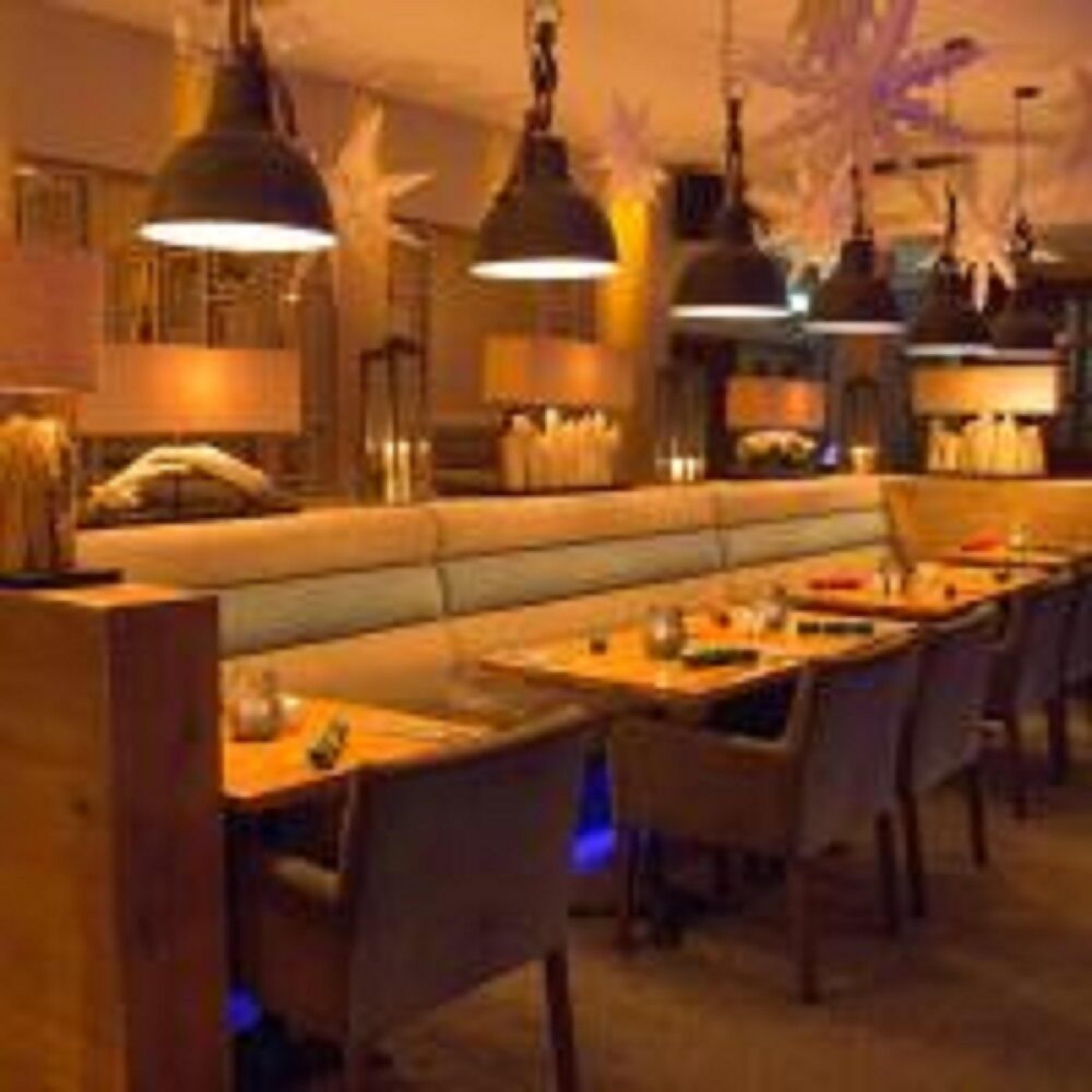A dimly lit restaurant with a long counter, multiple tables, and hanging pendant lights.