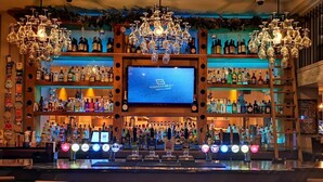 A bar area with a large screen displaying 'The Townhouse 211', multiple liquor bottles, and a variety of bar tools.