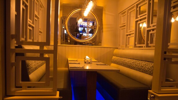 A dimly lit, cozy bar area with a circular mirror, cushioned seating, and a low table.