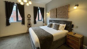 A bedroom with a large bed, a wooden nightstand, a wall clock, and a decorative wall piece.