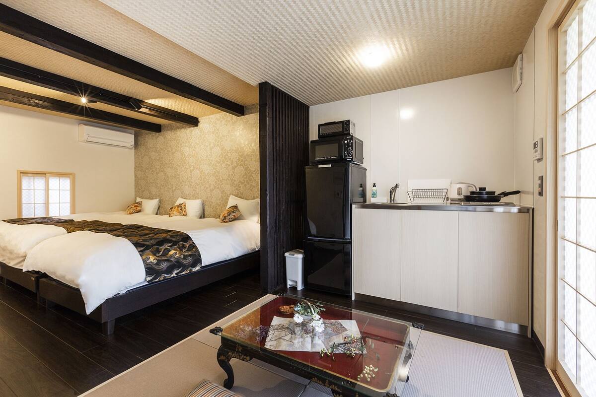 A hotel room with a bed, a small kitchenette, a dining table, and a window.