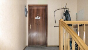 Une porte en bois avec une pancarte « Bienvenue », un porte-manteau avec une veste, et une rampe d’escalier en bois.