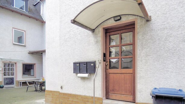 Une maison avec une porte d’entrée en bois, une boîte aux lettres et une poubelle.