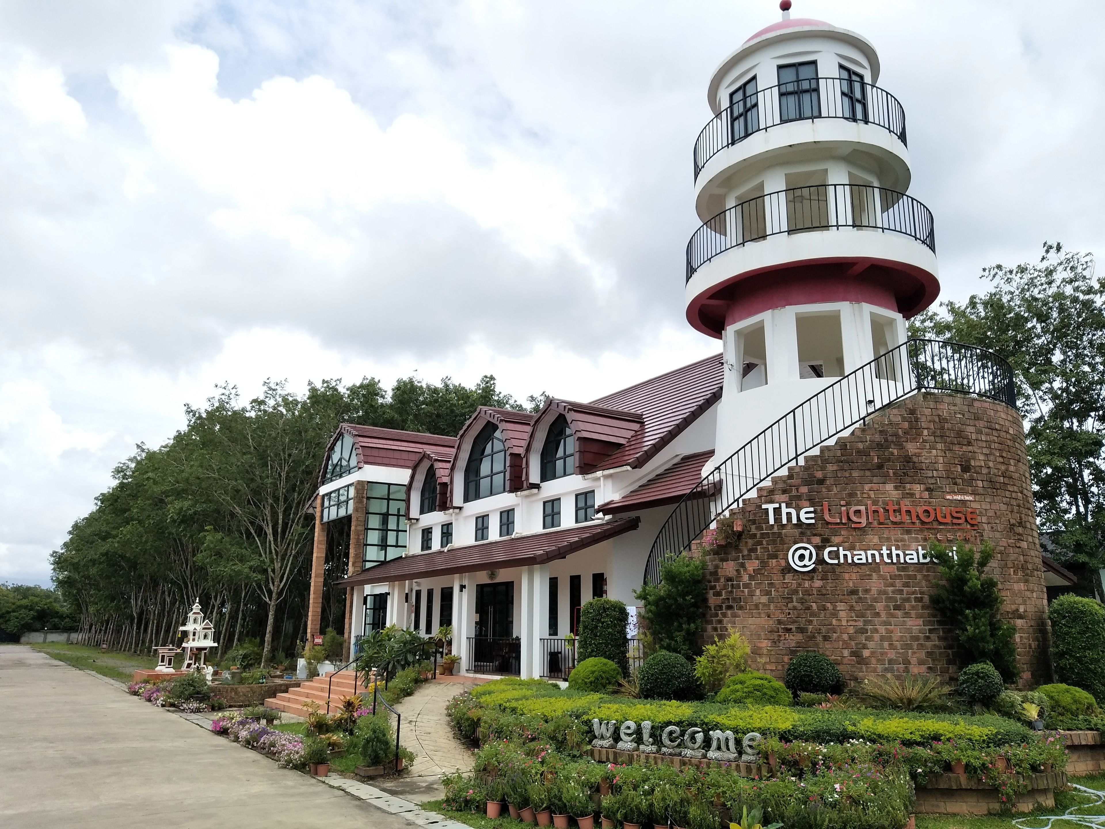 A building with a lighthouse tower, a welcoming sign, and a well-maintained garden.