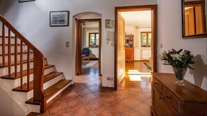 Eine Treppe führt zu einem Wohnbereich mit Holztreppe, gefliestem Boden und einer hölzernen Kommode mit Blumen in einer Vase.