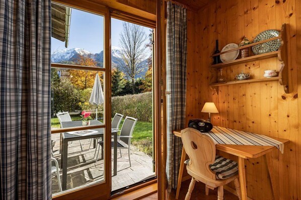 Un interior de madera con una mesa de comedor, sillas, una lámpara y una estantería con vajilla.