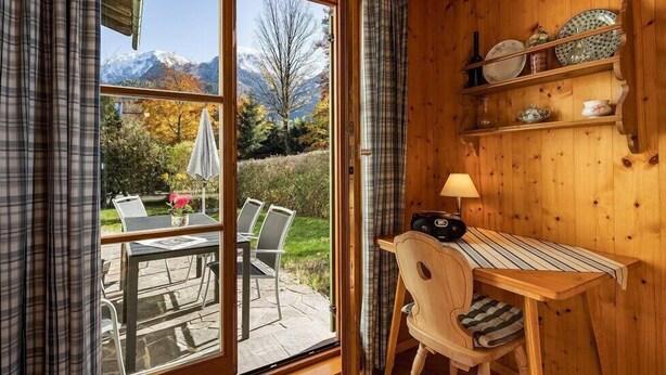 Eine Holzhütte mit Essbereich, einem Tisch mit Stühlen, einer Lampe und Regalen mit Geschirr.