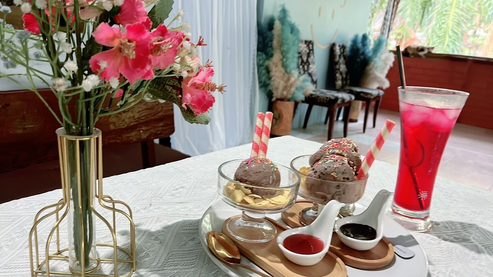 A table with a floral arrangement, three dessert cups, a glass of iced drink, and a white teapot.