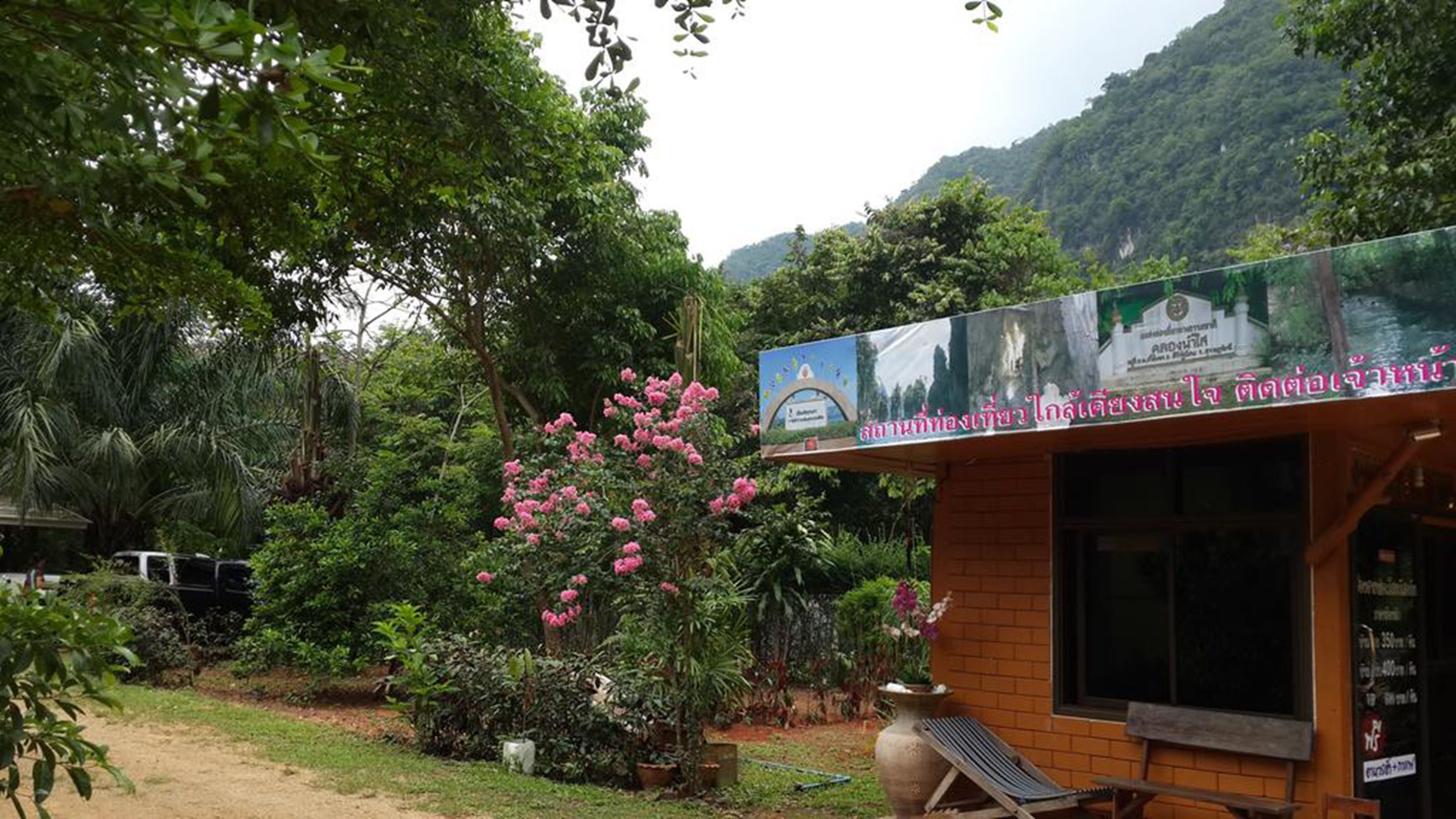 A small wooden structure with a signboard, surrounded by lush greenery and a mountain backdrop.