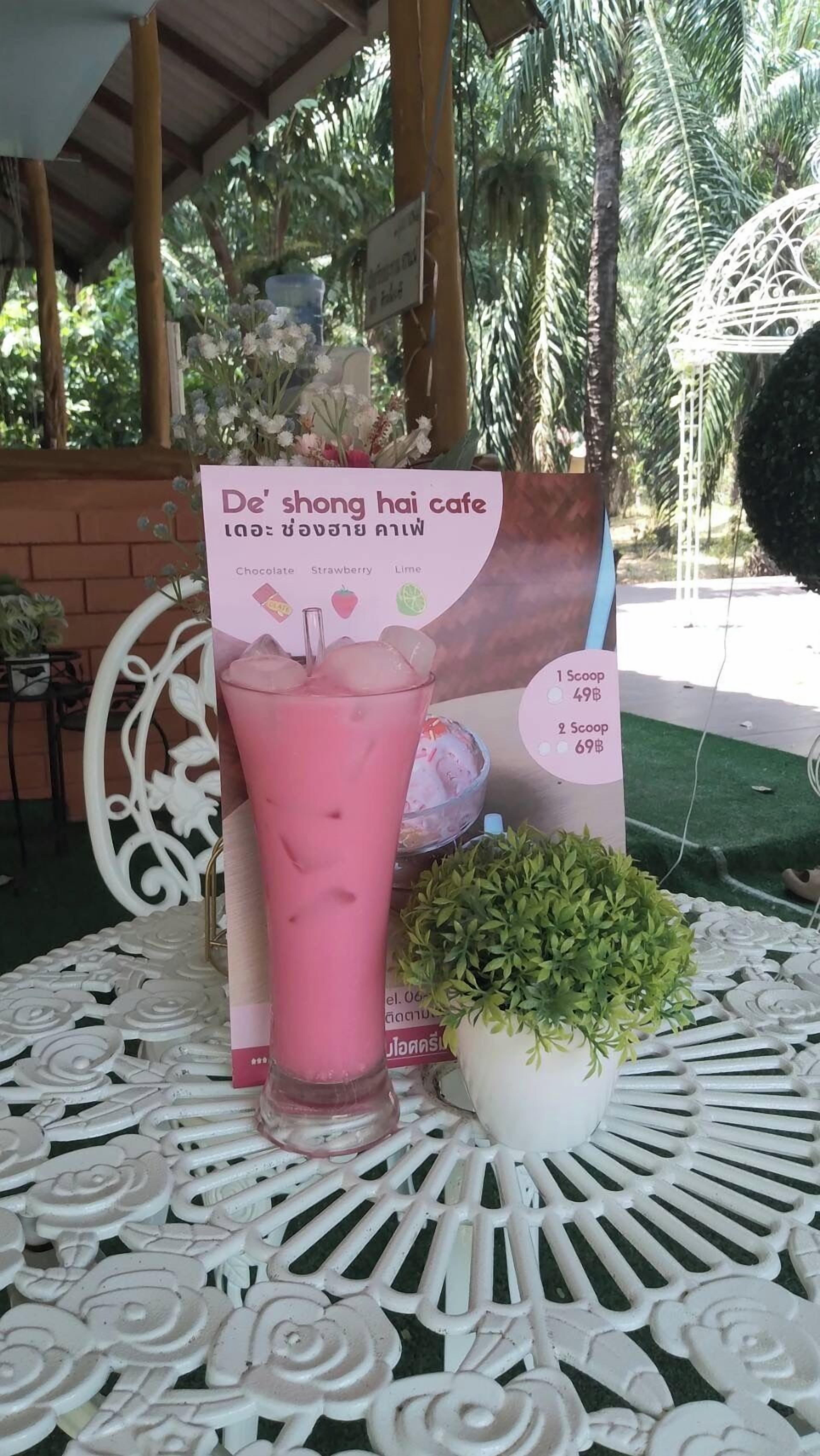 A table with a pink drink, a menu, and a small potted plant.