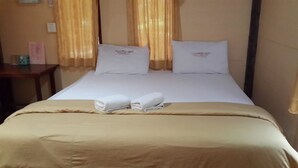 A hotel room with a bed, two pillows, a beige bedspread, and two folded towels.