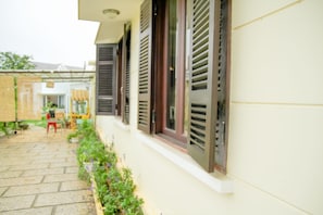 A building with a white exterior, a paved pathway, and a small garden area with plants and a red chair. - 69 Lugia House (Lam Vien - Da Lat)
