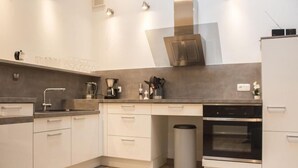 A modern kitchen with white cabinets, a stainless steel oven, and a coffee machine. - holiday flat (Siegsdorf)