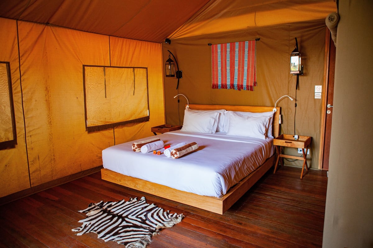 Une pièce aménagée comme une tente, avec un lit en bois, un tapis à motifs zébrés, une lanterne fixée au mur et un rideau rayé de rouge et de blanc.