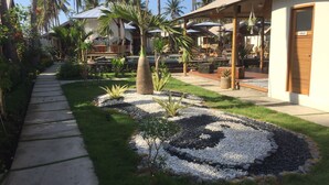 Un resort con un camino pavimentado, palmeras y zonas de estar al aire libre.