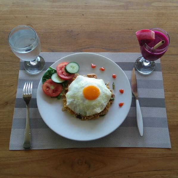 A plate with a fried egg on top of noodles, accompanied by a side salad and a glass of water.