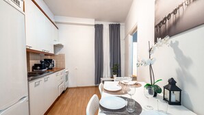 Una cocina compacta con armarios blancos, cafetera y zona de comedor con platos blancos, vasos y un farol negro.