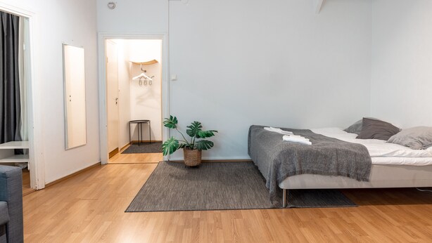 Un dormitorio moderno con cama, alfombra gris, planta en maceta y un pasillo que da a un baño.