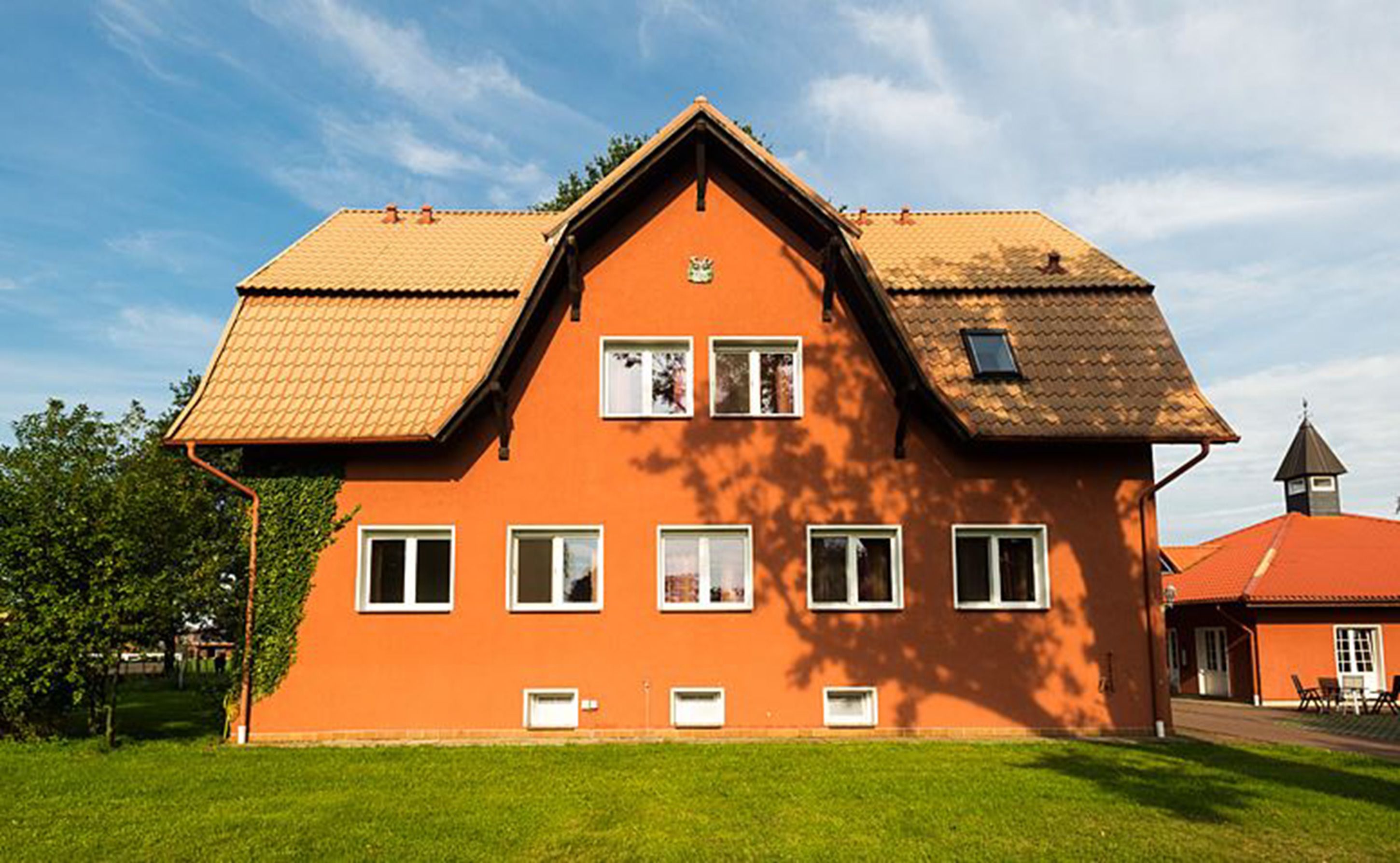 A large, orange house with a steeply pitched roof, multiple windows, and a small tower-like structure on the right.