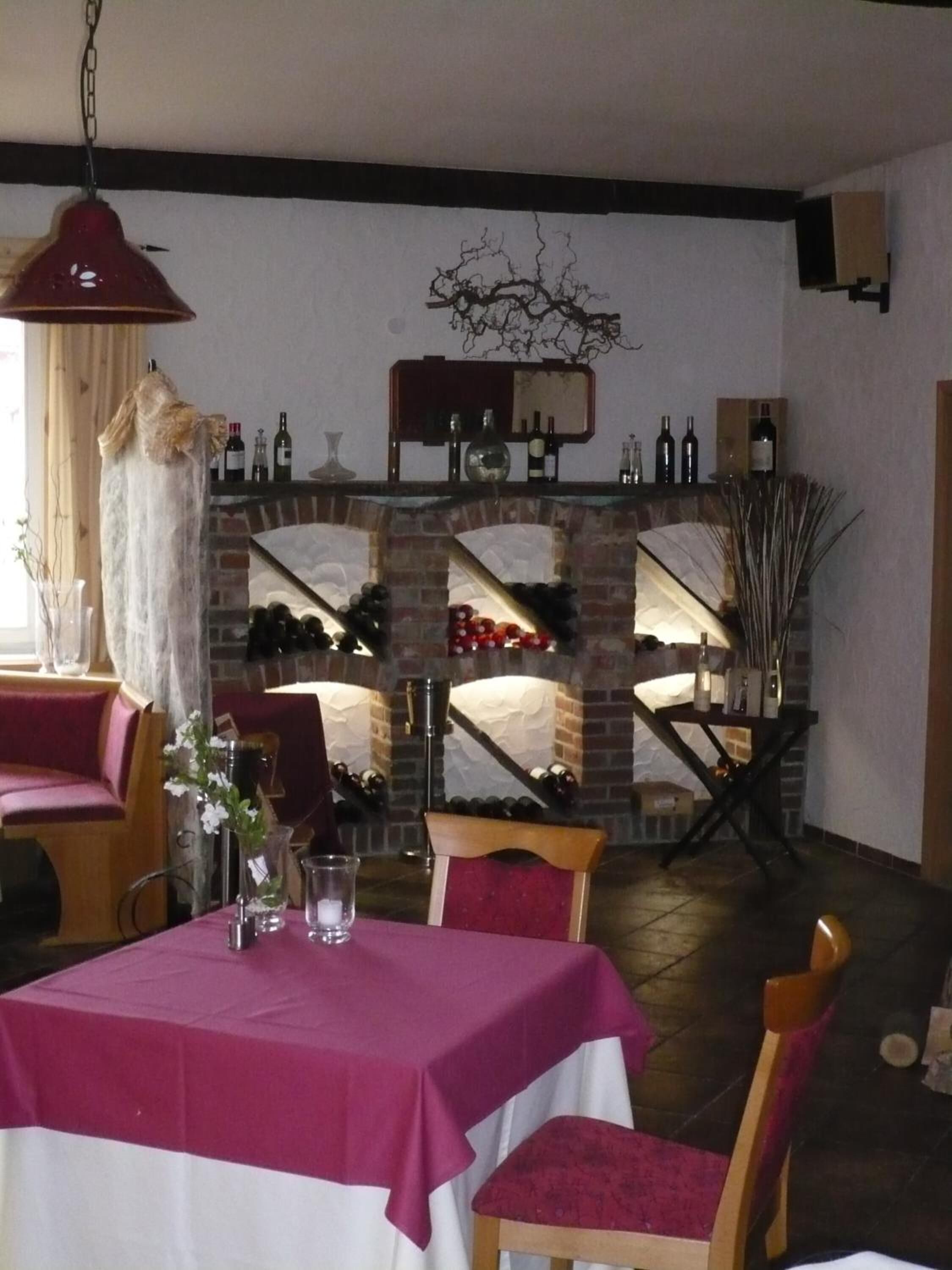 A dining area with a brick fireplace, wine bottles, and a table set with a tablecloth and chairs.