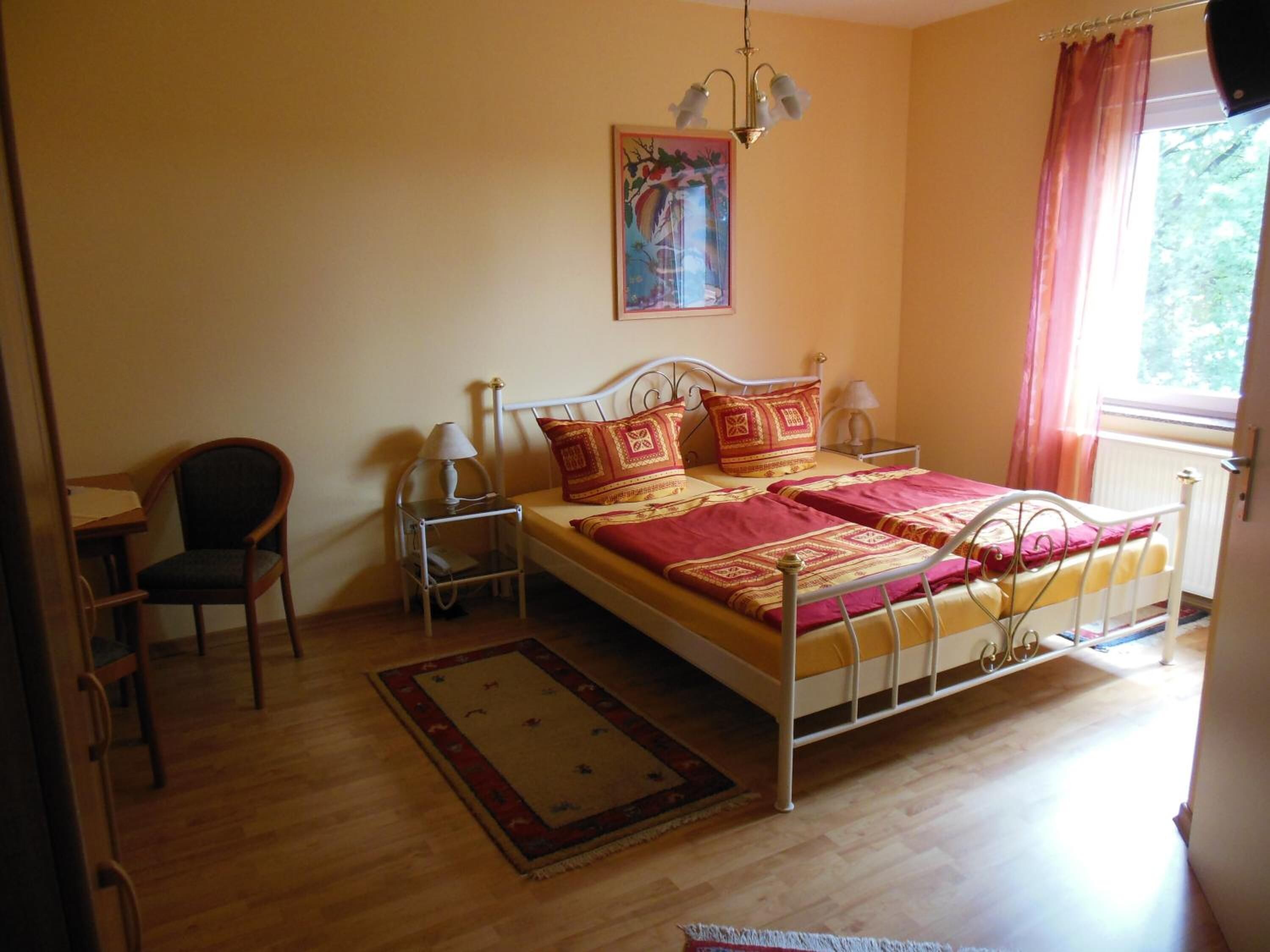 Een slaapkamer met een bed, een stoel, een bureau en een raam met gordijnen.